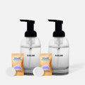The BLUELAND Hand Soap Starter 2-Pack includes two clear reusable glass dispensers with black pumps, each with a Foaming Hand Soap Lavender Eucalyptus packet and plastic-free tablets, all shown on a plain white background.