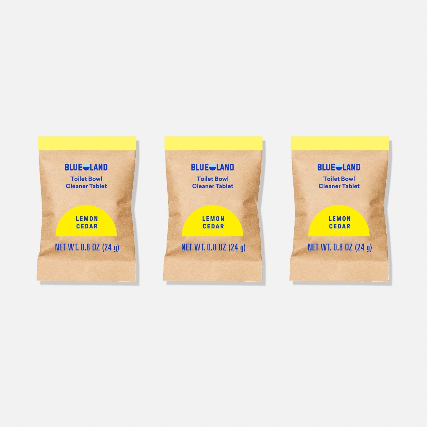 Three brown packets of the Toilet Bowl Cleaner Sample Pack (3 Tablets) in Lemon Cedar scent stand upright, showcasing one round white tablet. The packaging features a yellow circle and is simple and plastic-free, emphasizing the products eco-friendly design.