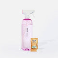 A clear spray bottle labeled “Blueland Bathroom” filled with pink liquid stands beside a small brown packet labeled Blueland Eucalyptus Mint Cleaner Tablet and a pink cleaning tablet.